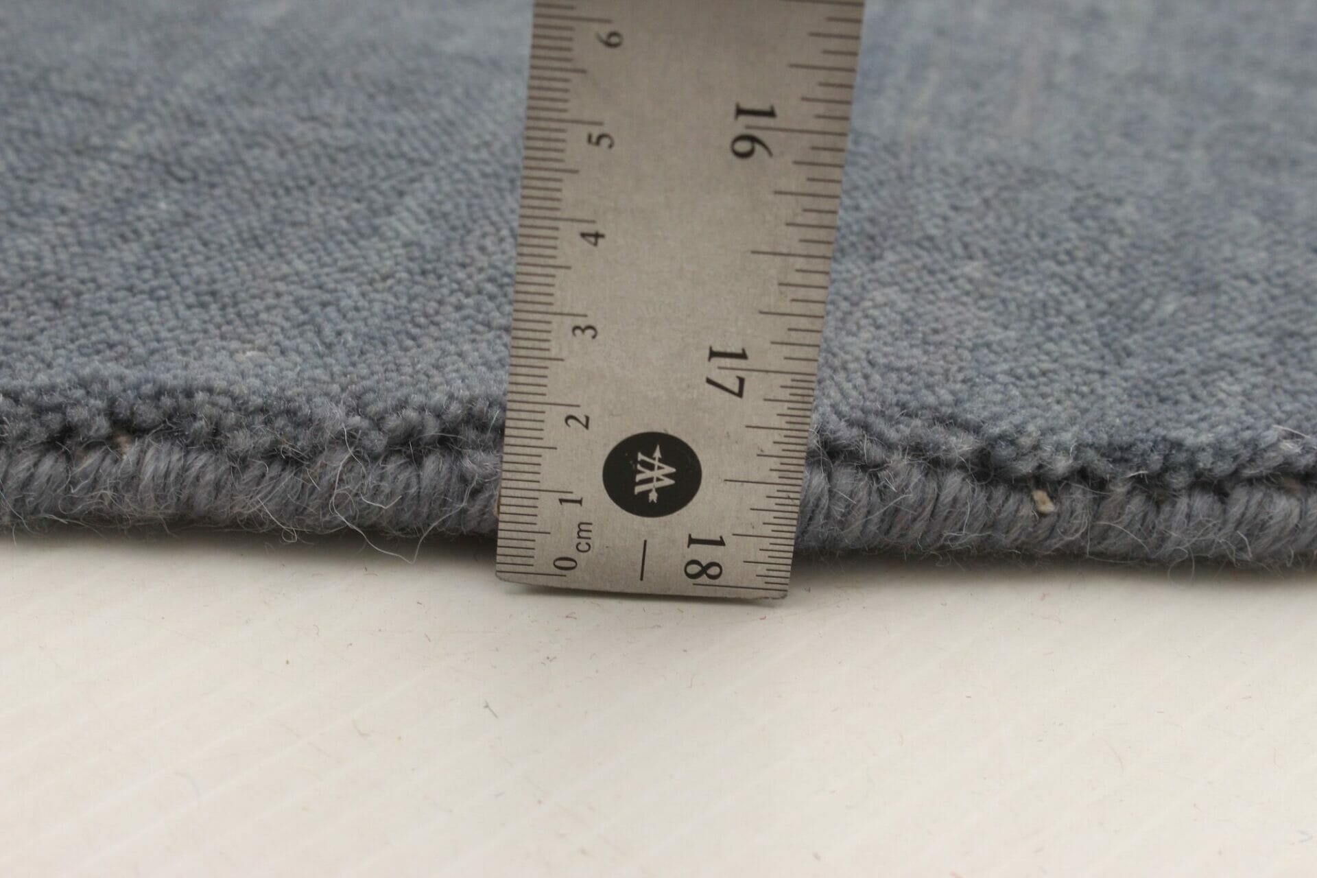 Een vloerkleedliniaal wordt gebruikt om de lengte van een blauwe stof te meten.