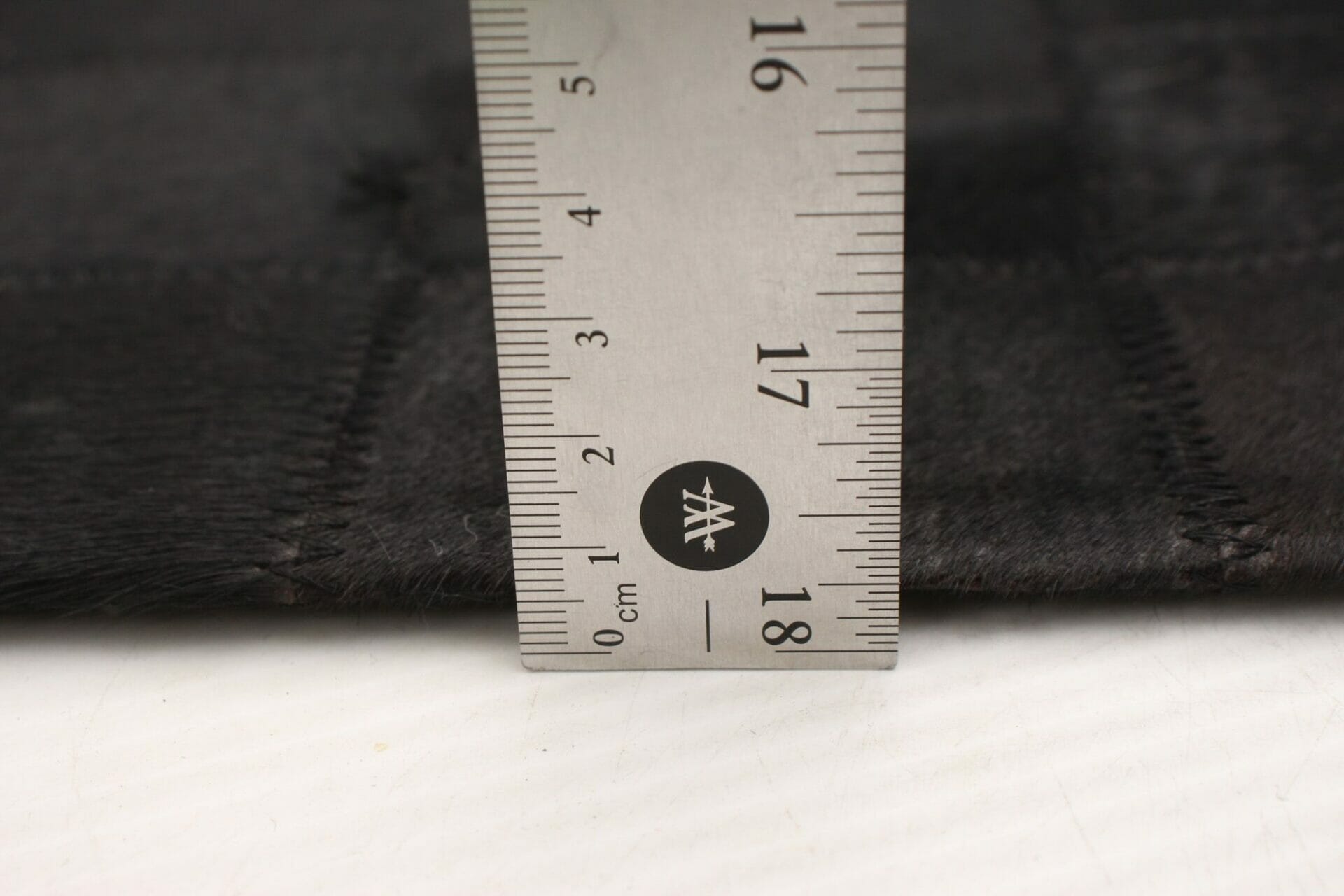 Een vloerkleedliniaal wordt gebruikt om de lengte van een zwarte bonttapijtstof te meten.