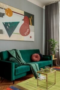 Een woonkamer met een groene bank, een kleurrijk schilderij en een vloerkleed.