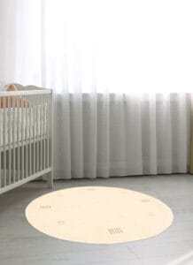 Een babykamer met een wit wiegje en een rond vloerkleed.