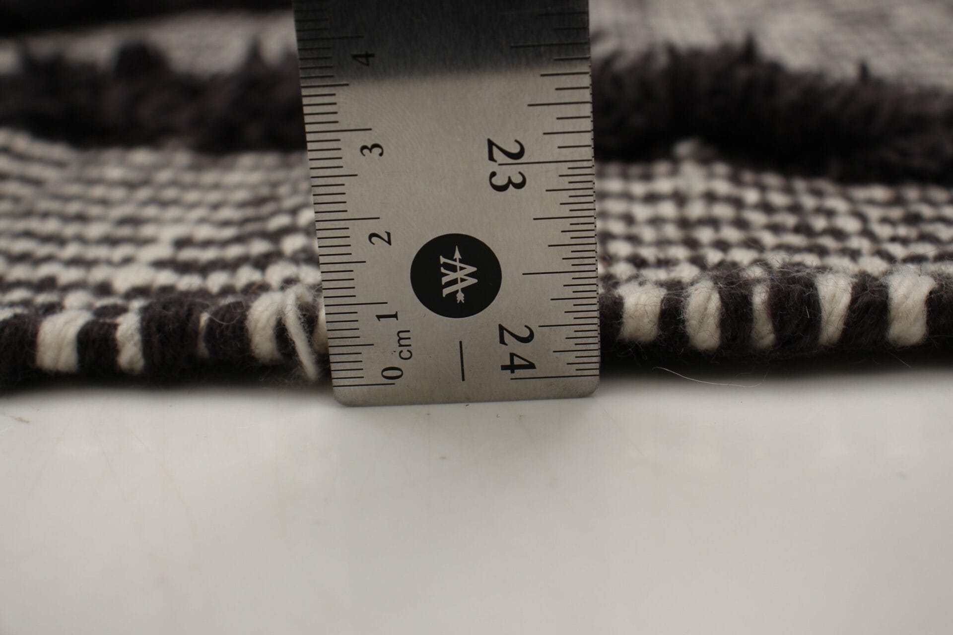 Een close-up van een liniaal op een zwart-wit tweed stoffen vloerkleed.