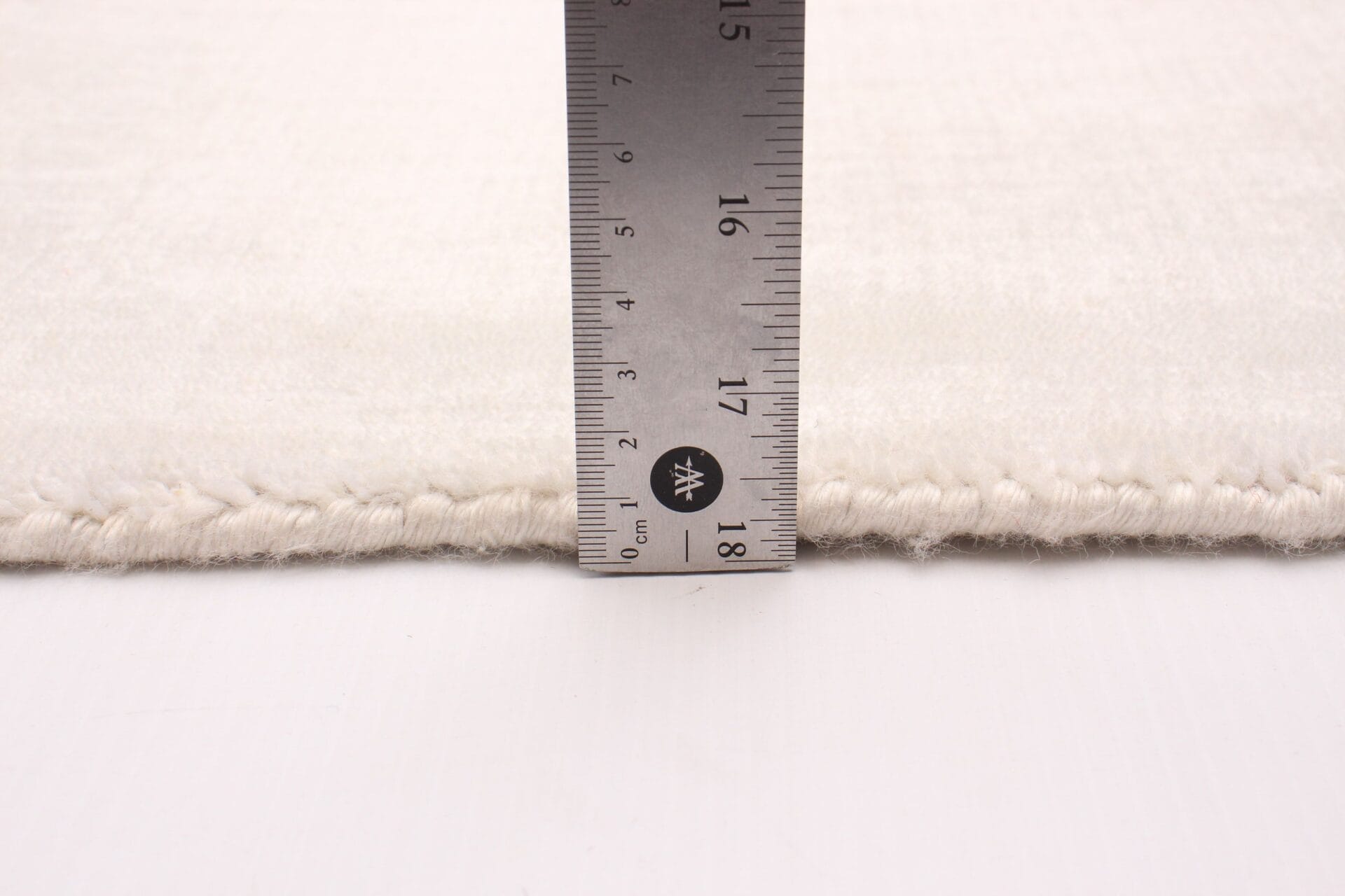 Voor het meten van de lengte van een wit vloerkleed wordt een liniaal gebruikt.