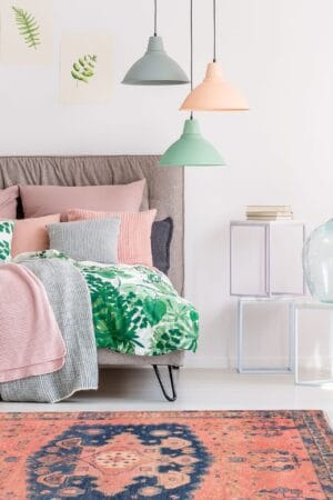 Een slaapkamer met een roze, groen en blauw vloerkleed.