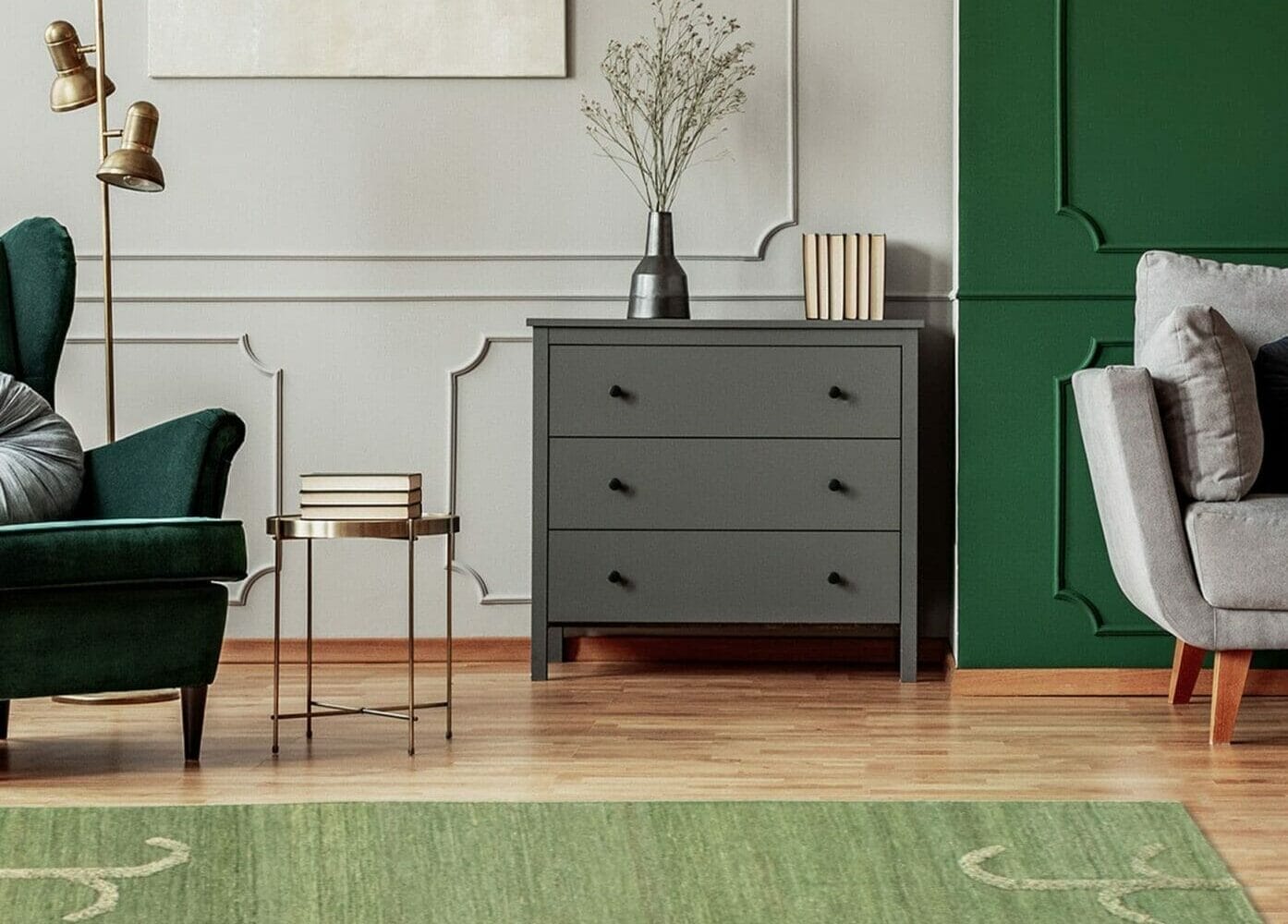 Een woonkamer met een groene fauteuil, een grijs dressoir en ingelijste kunst aan de muur. Boven ons staat rechts een grijs gestoffeerde fauteuil en op de houten vloer ligt een groen tapijt.