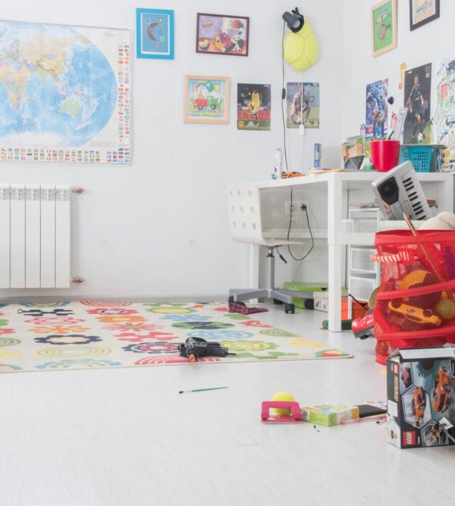 Een kinderslaapkamer met een doordachte babykamerindeling met links een bed, rechts een bureau en verspreid op de vloer divers speelgoed. Aan de muren hangen kaarten, posters en charmante tekeningen.