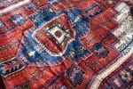 Een close-up van een kleurrijk Perzisch tapijt met ingewikkelde geometrische patronen in rood, blauw, wit en een vleugje groen. Zorg ervoor dat de levendige schoonheid behouden blijft door eventuele oude vervuilingen op de juiste manier te verwijderen.