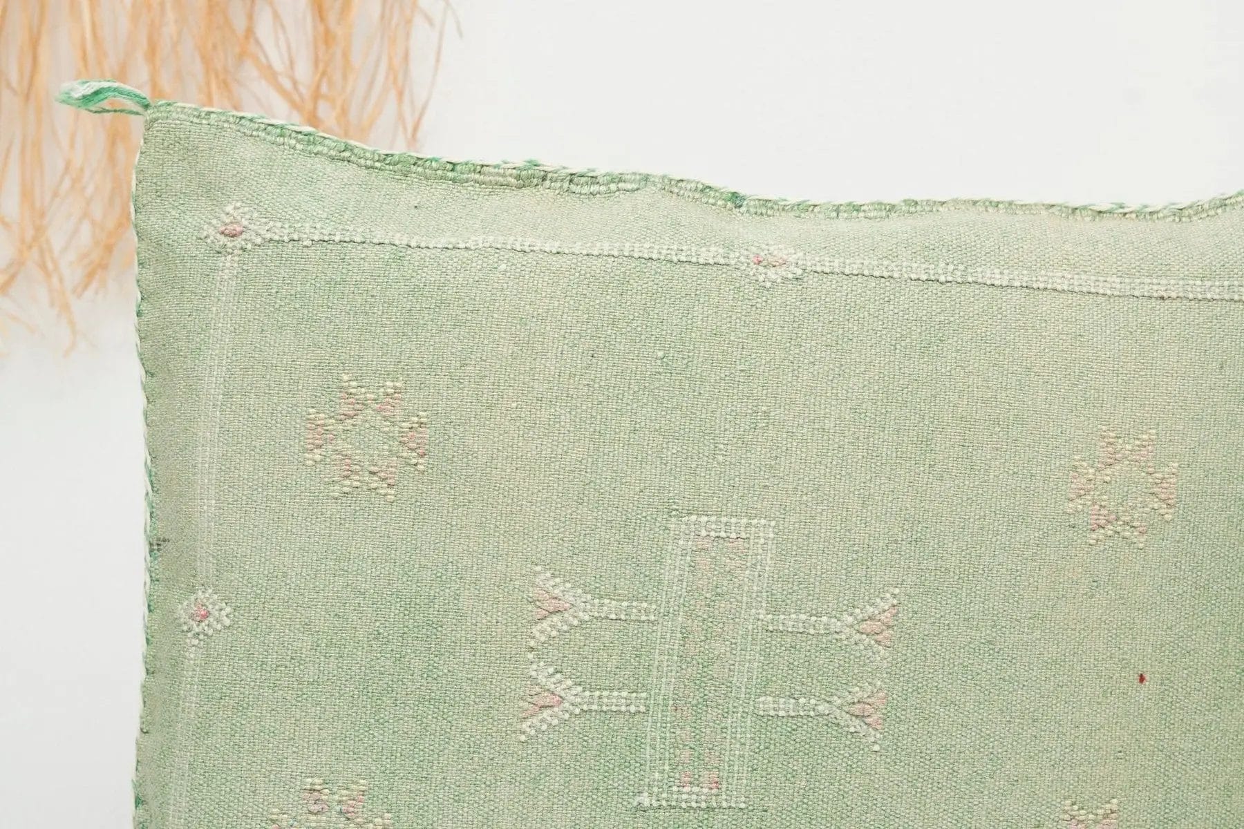 Close-up van een groene stof met subtiele geometrische patronen in wit en roze, naast beige kwastjes.