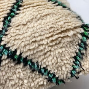 Close-up van een crèmekleurige stof met een structuur en een zwart-groen ruitpatroon.
