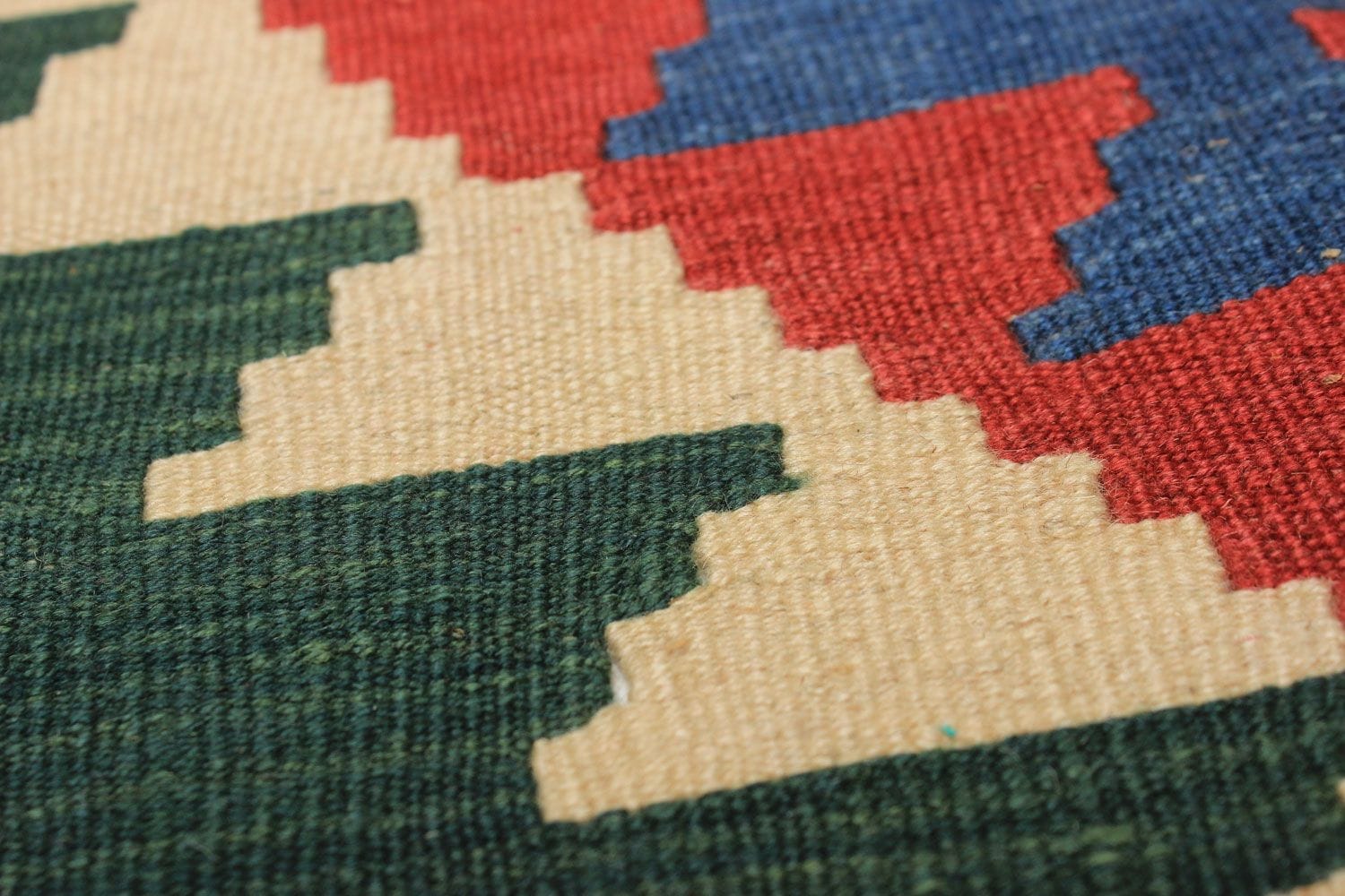 Close-up van een geweven textiel met een geometrisch zigzagpatroon in de kleuren rood, blauw, groen en beige.