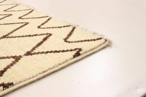 Een hoek van een beige tapijt met bruine zigzagpatronen op een gladde, lichtgekleurde vloer.
