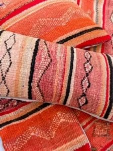 Close-up van het Vintage Kilim kussen - rood en oranje divers, met levendige, handgeweven textiel in tinten rood, oranje en roze met ingewikkelde geometrische patronen, gerangschikt in meerdere lagen, wat lijkt op een rijk gekleurd tapijt.