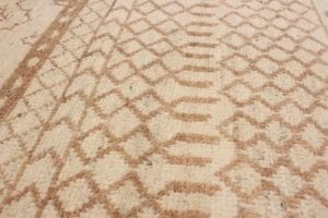 Close-up van een beige geweven tapijt met een geometrisch bruin patroon.