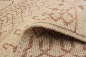Close-up van een beige en bruin tapijt met een patroon, met een zichtbare vouw die de textuur en geweven details laat zien.