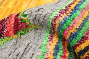 Close-up van een kleurrijke, gestructureerde stof met een grijze basis, met levendige rode, groene, gele, blauwe en roze patronen.