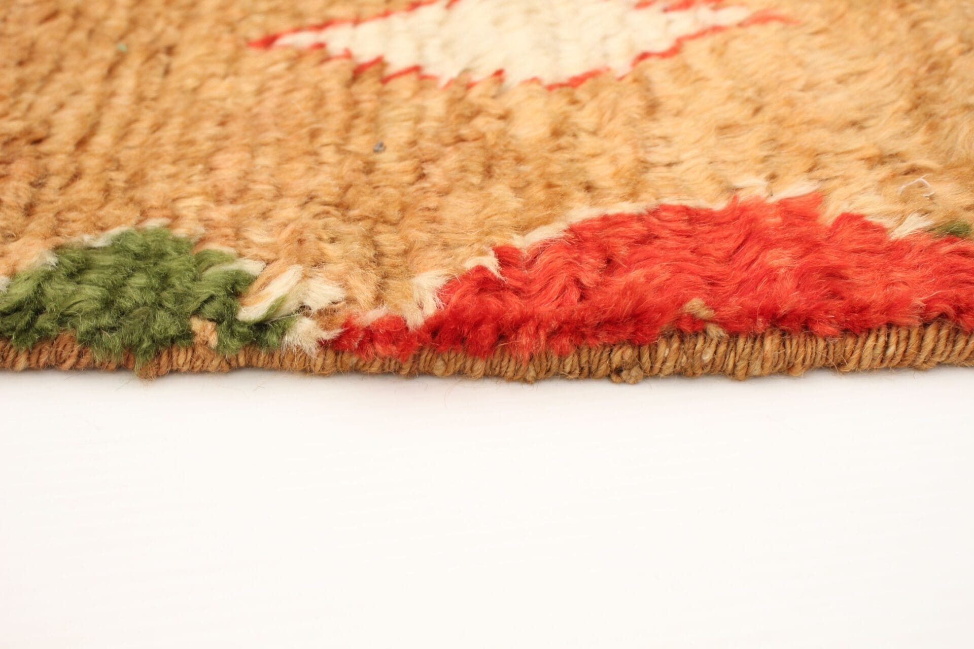 Close-up van een geweven tapijt met een getextureerde rand met groene, beige en rode patronen.