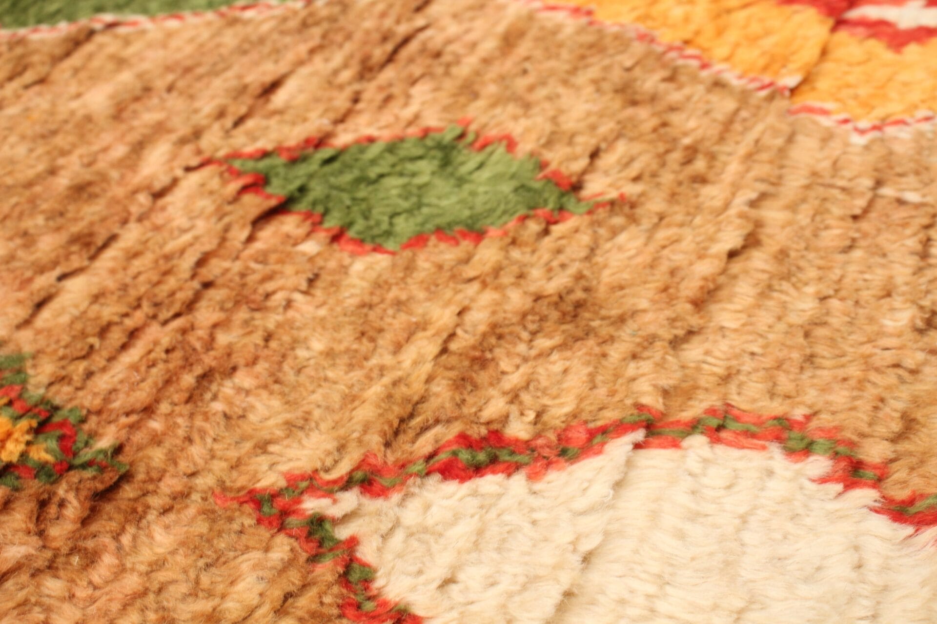 Close-up van een geweven tapijt met een patroon van aardse tinten, met groene en beige ruitvormen, omlijnd met rood.
