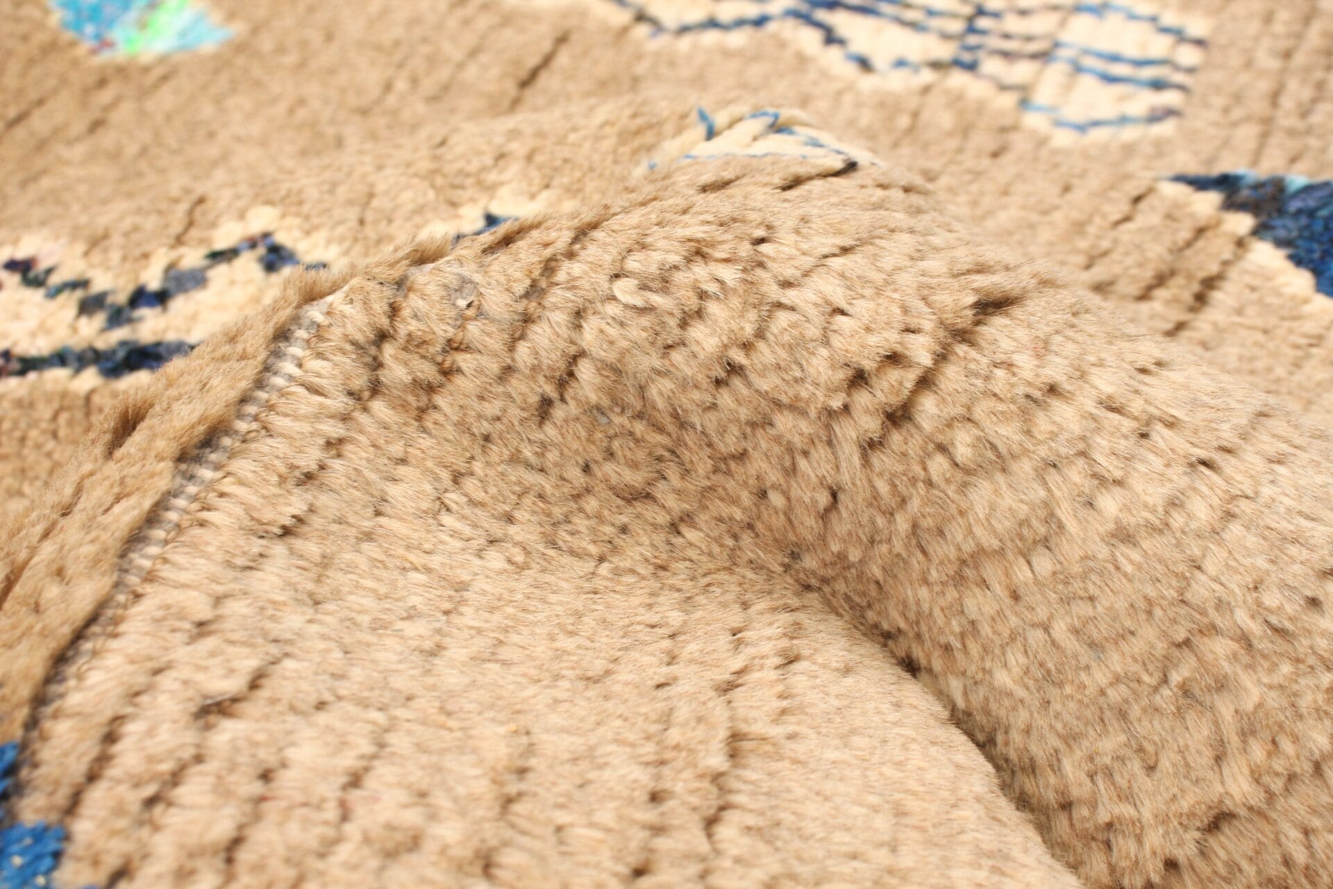 Close-up van een geweven stof in beige en blauw met onregelmatige patronen en opstaande draden.