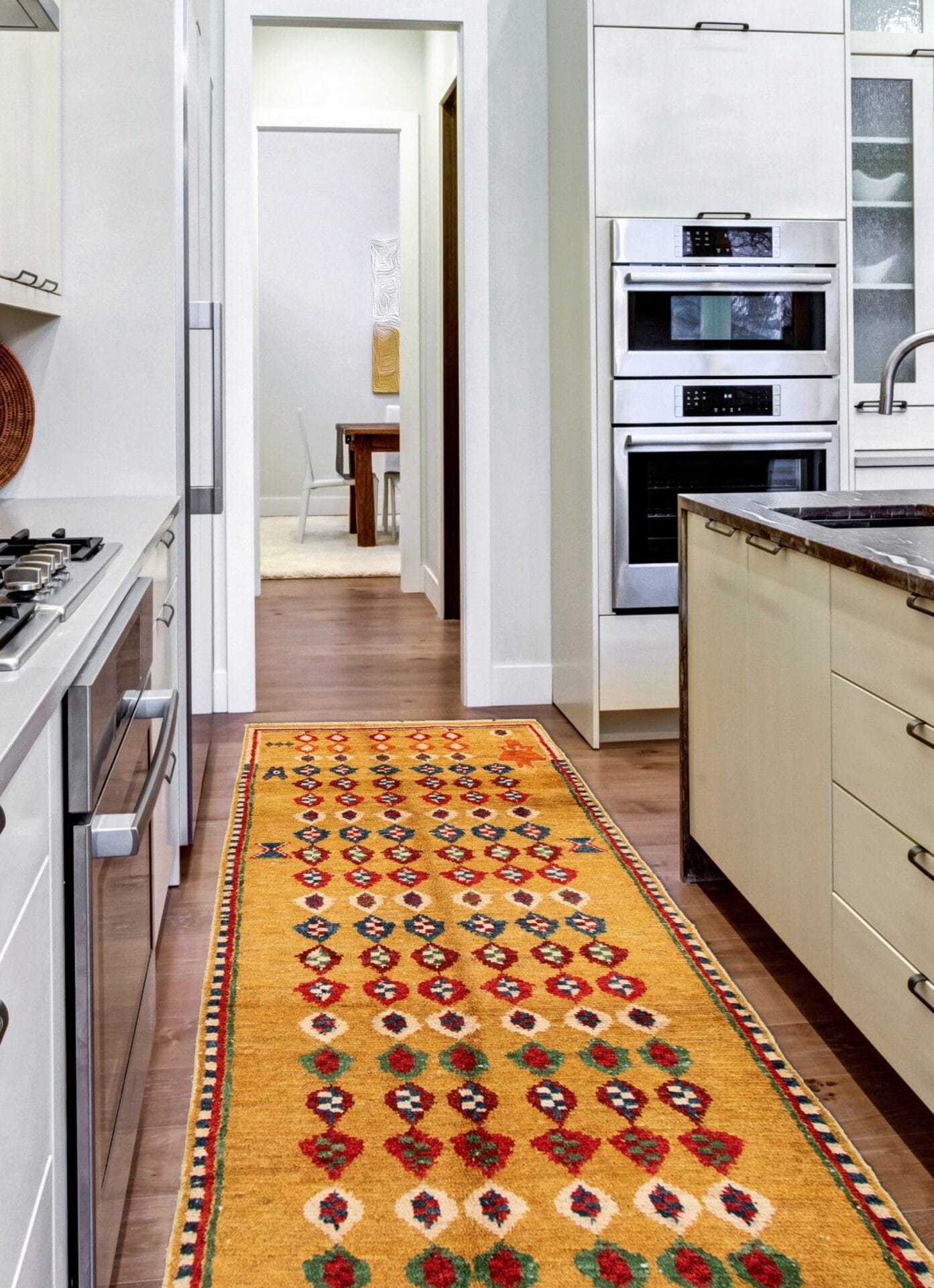 Een moderne keuken met witte kasten, roestvrijstalen apparaten en een kleurrijk patroon op de vloer. Een kookeiland met een donker aanrechtblad staat in het midden. Eetgedeelte zichtbaar op de achtergrond.