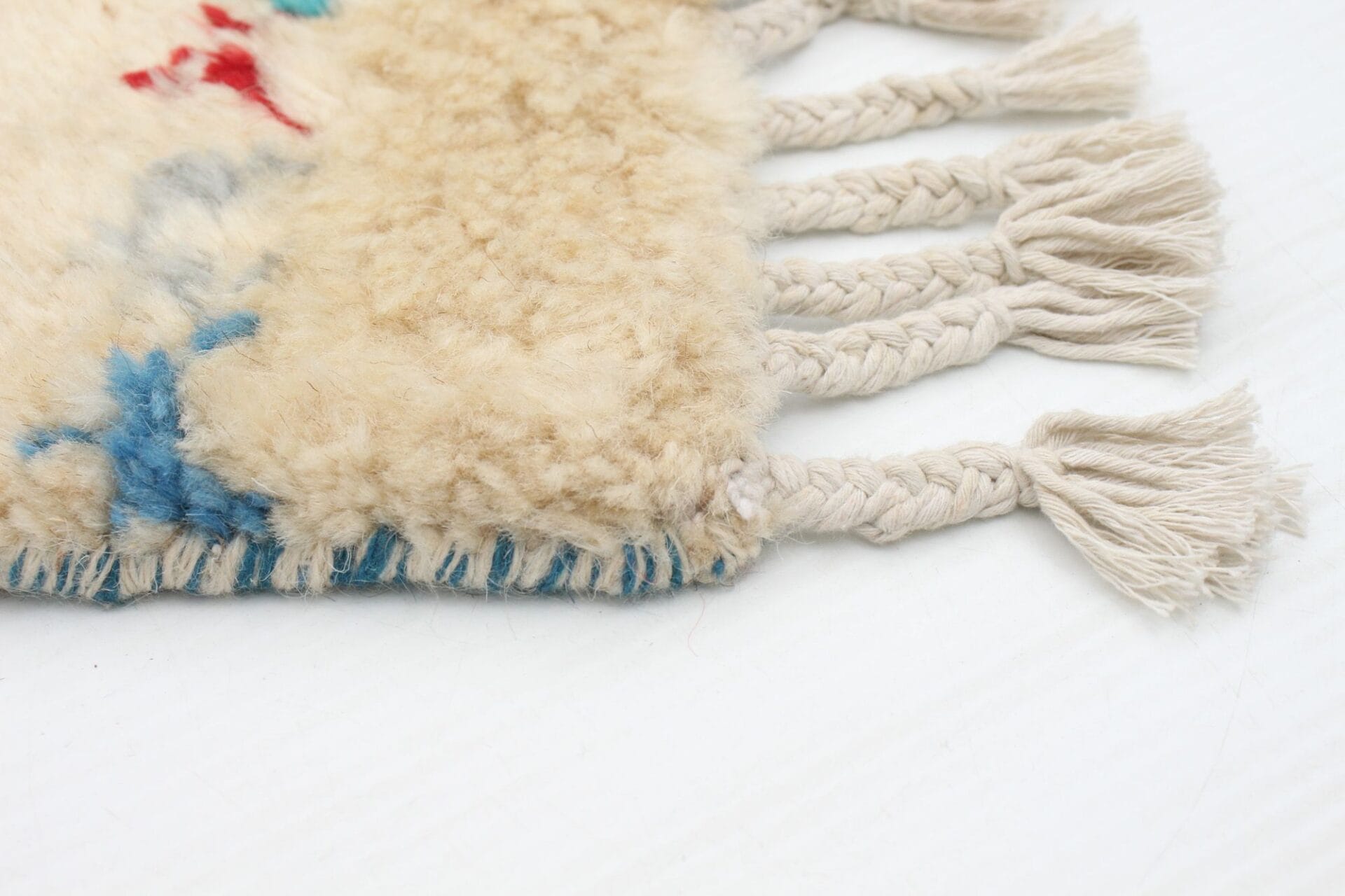 Close-up van een hoek van een geweven beige en blauw tapijt met gevlochten franjes op een licht oppervlak.