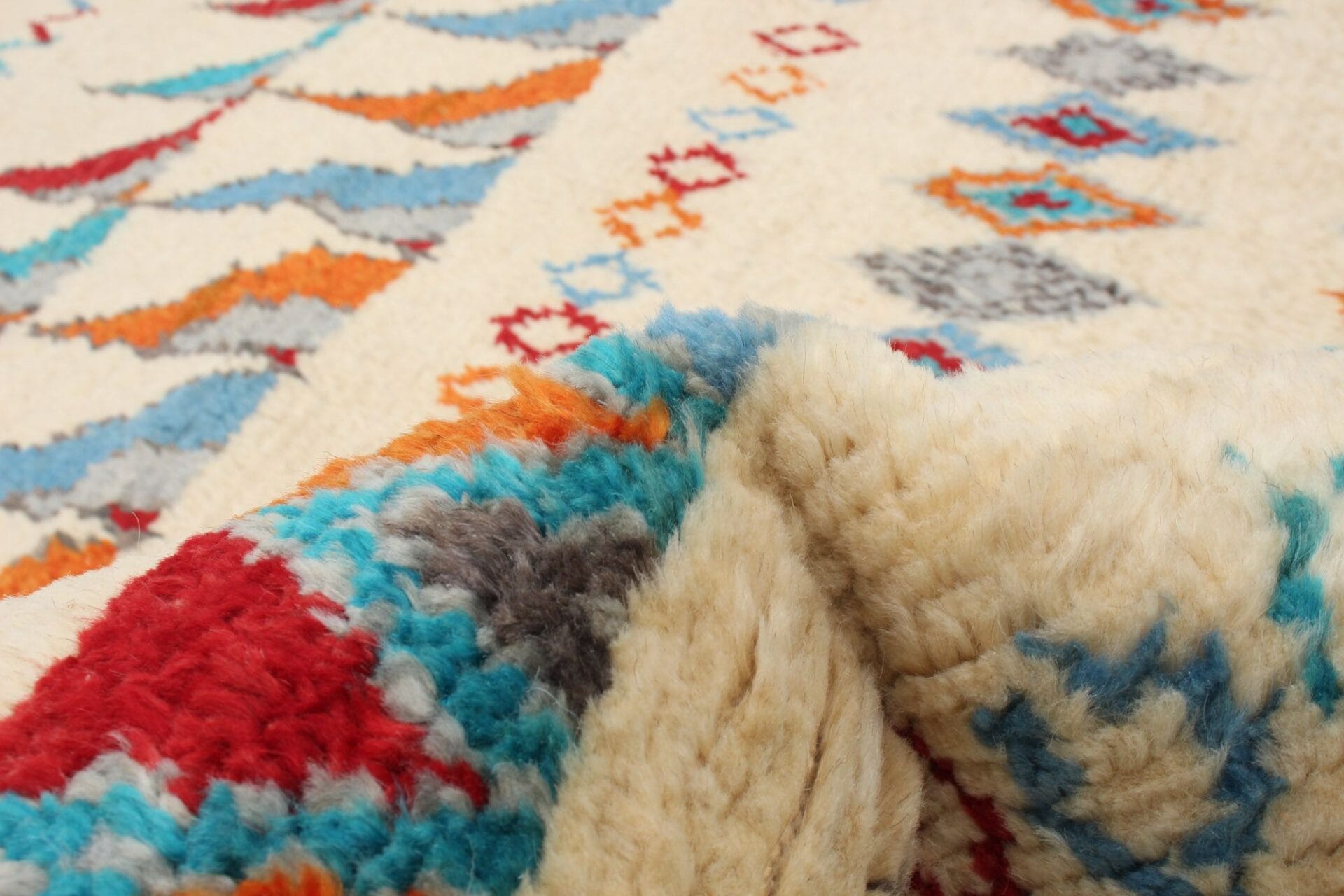 Close-up van een kleurrijk wollen tapijt met geometrische patronen in rood, blauw en oranje op een crèmekleurige achtergrond.