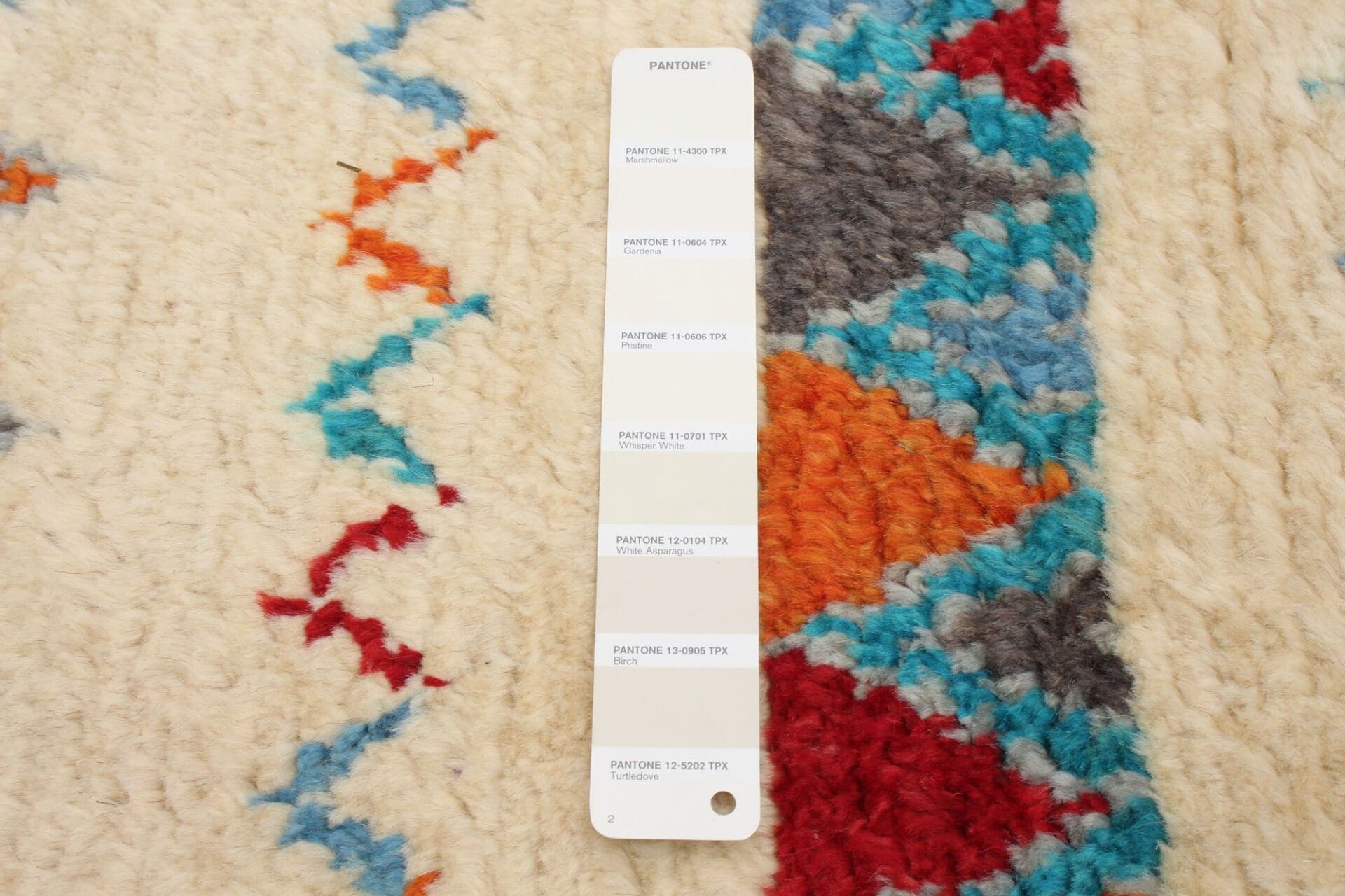 Een Pantone-kleurenstaalkaart op een kleurrijk vloerkleed met een zigzagpatroon.