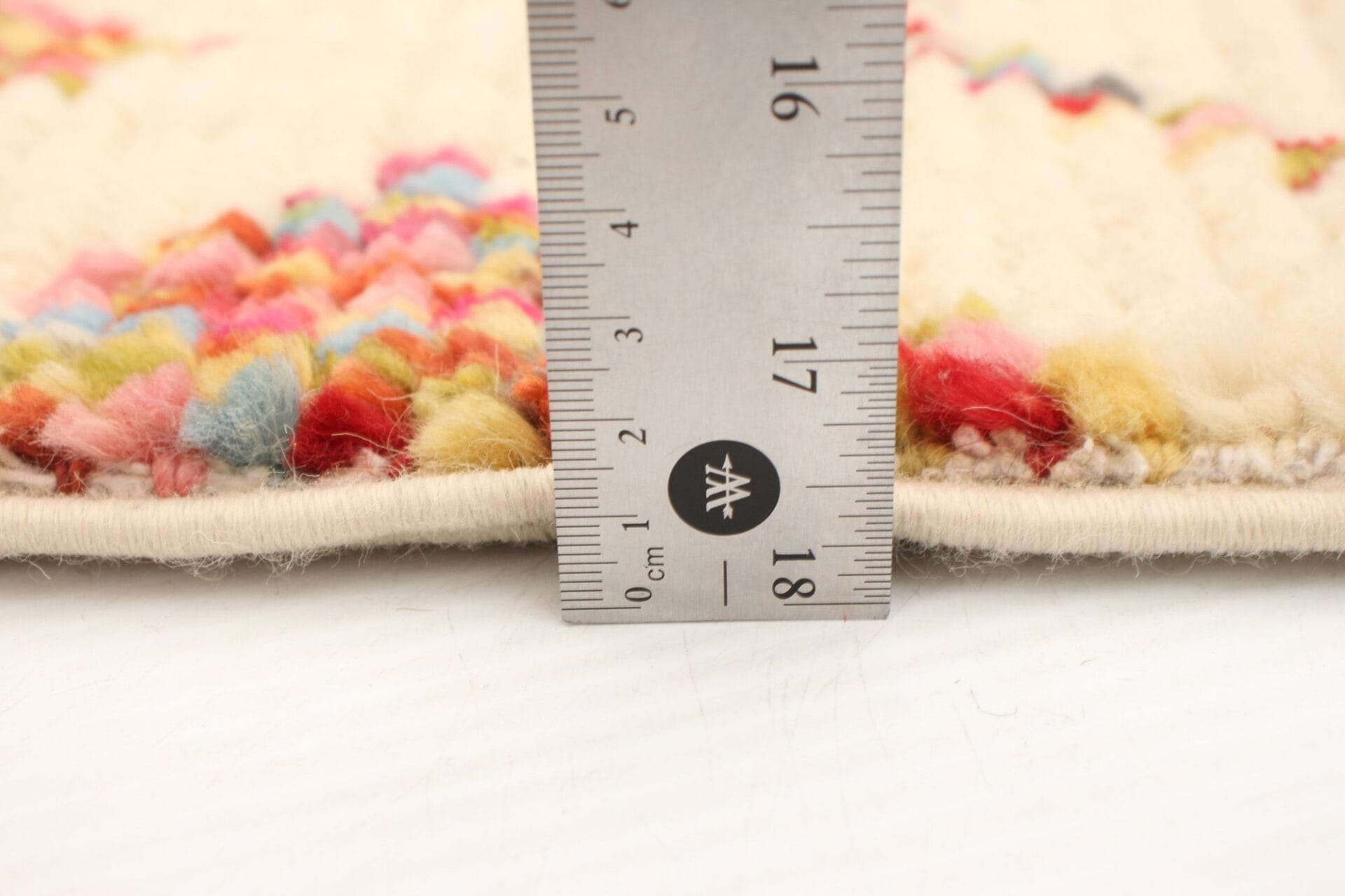 Een liniaal die de dikte van een veelkleurige geweven stof meet, met een dikte van ongeveer 1,5 cm.