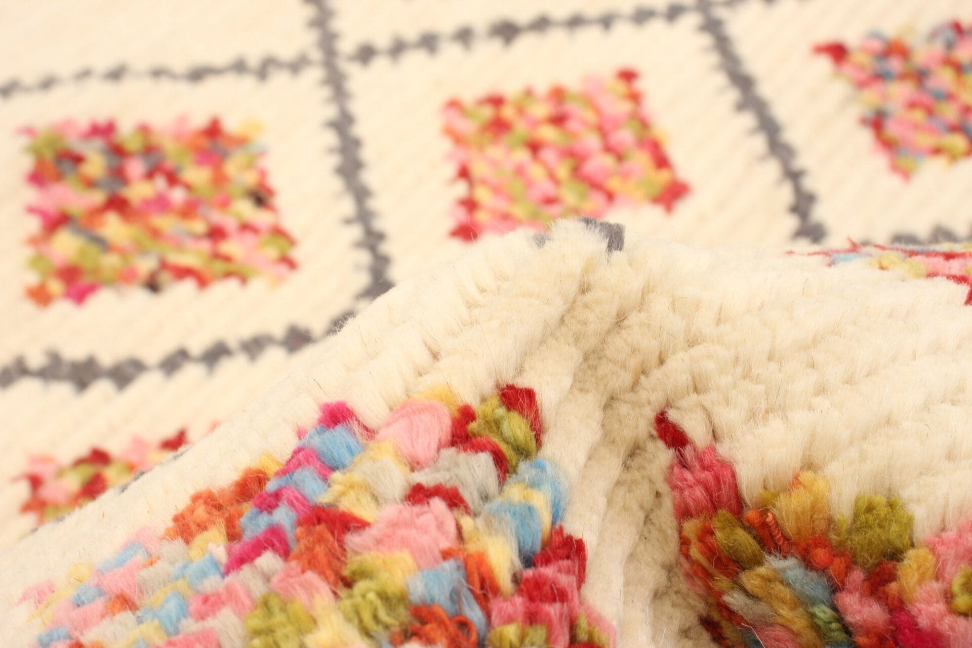 Close-up van een wollen textiel met kleurrijke geometrische patronen op een crèmekleurige achtergrond.