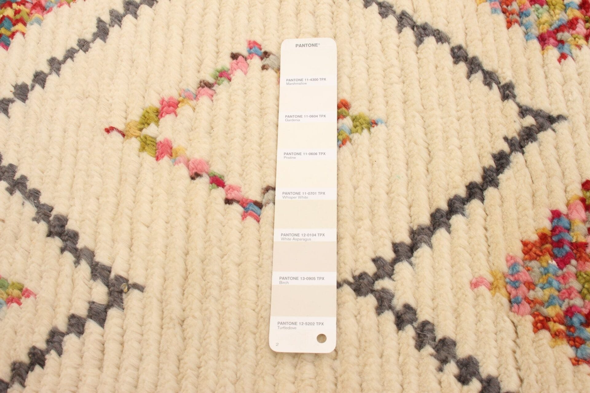 Een Pantone-kleurenstaalkaart met zes tinten wordt op een gestructureerde, veelkleurige geweven stof gelegd.