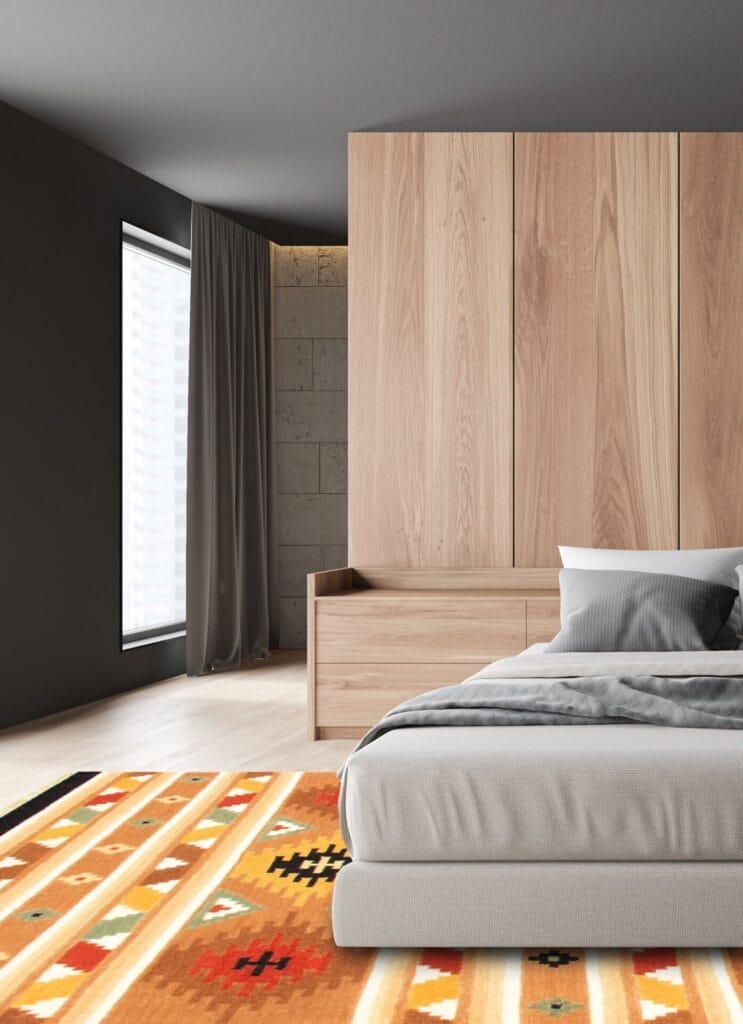 Moderne slaapkamer met een grote houten kledingkast, grijs bed met wit en grijs beddengoed en een oranje kleed met patroon. Grijze gordijnen bedekken een raam aan de linkerkant.