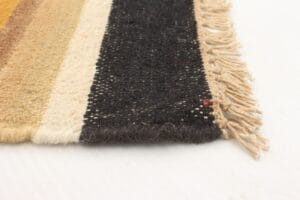 Close-up van een geweven stof met franjeranden, met horizontale strepen in tinten bruin, beige en zwart.