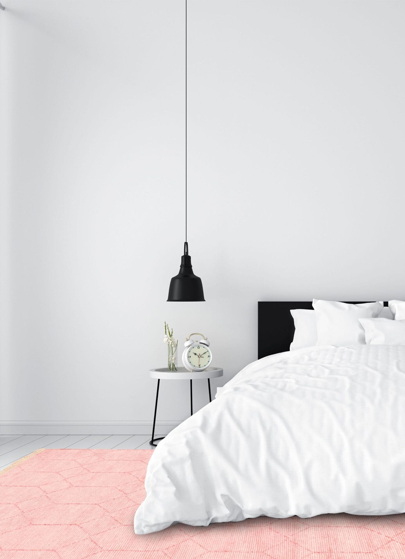 Minimalistische slaapkamer met witte muren, een wit bed en een zwart hoofdeinde. Op een klein rond nachtkastje staan een witte wekker en een plant. Boven de tafel hangt een zwarte hanglamp en op de vloer ligt een roze vloerkleed.