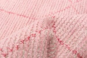 Close-up van een roze gebreide stof met een structuurpatroon en zichtbare steken.