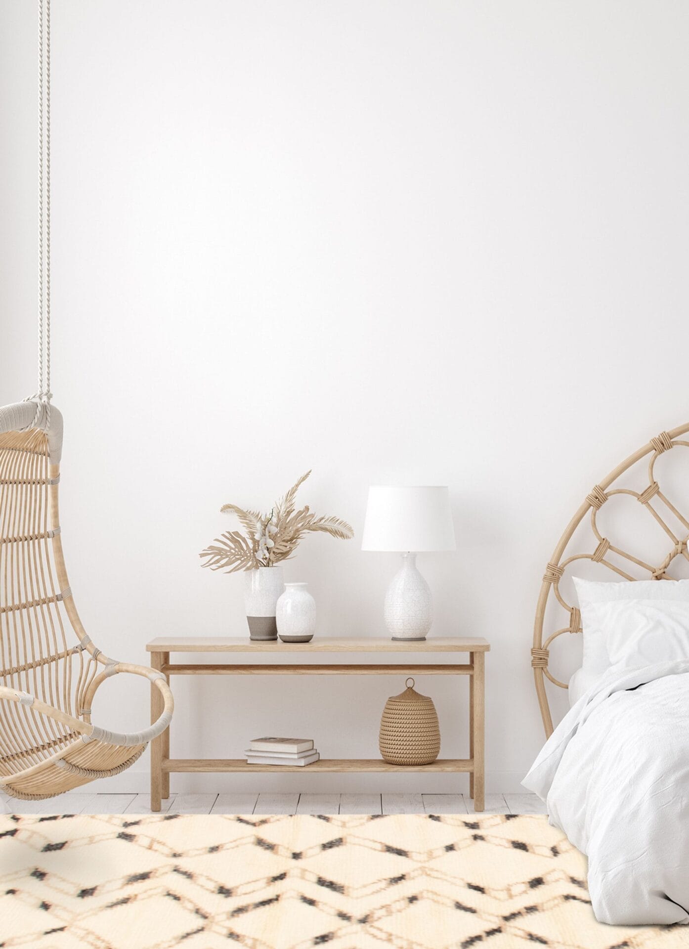 Minimalistische slaapkamer met een hangstoel, een houten bijzettafel met een lamp en decoratieve spullen, en een bed met een rieten hoofdeinde. Een zacht vloerkleed complementeert de witte muren en het lichtgekleurde decor en creëert een rustgevende sfeer.