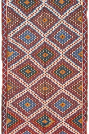 De Turkse Konya plat geweven wollen kelim, met een afmeting van 173 x 302 cm, is een rechthoekig vloerkleed versierd met traditionele ruitpatronen en ingewikkelde ontwerpen, met een mix van aardse kleuren zoals rood, blauw, wit en groen.