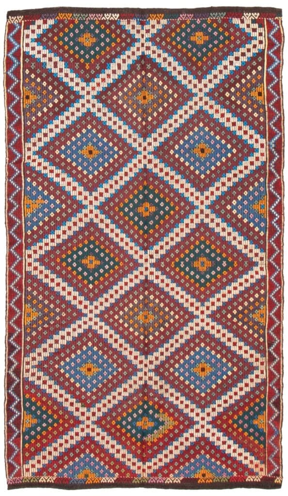 De Turkse Konya plat geweven wollen kelim, met een afmeting van 173 x 302 cm, is een rechthoekig vloerkleed versierd met traditionele ruitpatronen en ingewikkelde ontwerpen, met een mix van aardse kleuren zoals rood, blauw, wit en groen.