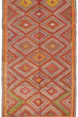 Een rechthoekige "Turks Konya plat geweven wollen wandtapijt kelim" van 183 x 325 cm heeft een ingewikkeld geometrisch patroon met ruitvormen in verschillende kleuren, waaronder oranje, rood, geel en groen. Dit vloerkleed heeft een mix van heldere en gedempte tinten.