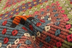 Een close-up van een kleurrijk, geweven textieltapijt met een patroon van kleine ruitvormen in verschillende kleuren, zoals rood, blauw, groen, roze en wit.