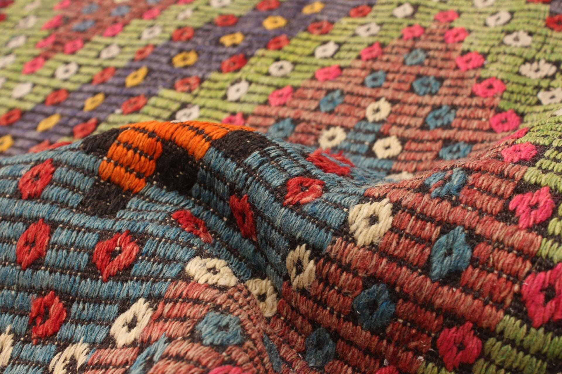 Een close-up van een kleurrijk, geweven textieltapijt met een patroon van kleine ruitvormen in verschillende kleuren, zoals rood, blauw, groen, roze en wit.