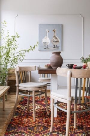 Een gezellige eethoek met een houten tafel en stoelen, een kleurrijk vloerkleed, potplanten en een muurschildering van twee eenden.