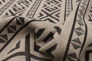 Close-up van beige stof met zwarte geometrische patronen, waaronder driehoeken en ruiten, waardoor een textuur ontstaat.