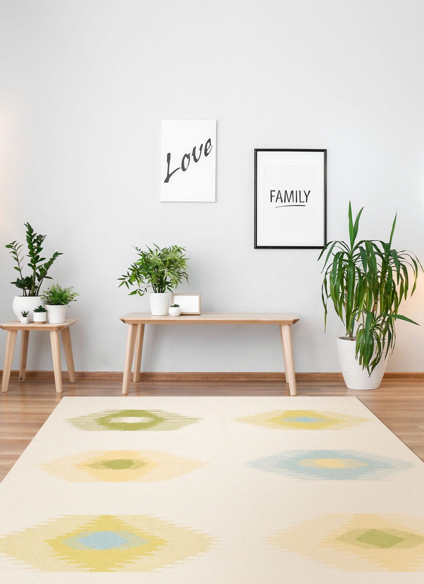 Minimalistische woonruimte met twee houten banken, diverse potplanten en ingelijste ‘Love’- en ‘Family’-kunstwerken aan de muur. Lichtgekleurd vloerkleed met patroon op de houten vloer.