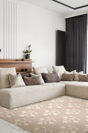 Een moderne woonkamer met een beige sectionele bank met meerdere kussens in neutrale tinten, een kleine plant op een houten plank, donkere kamerhoge gordijnen en een beige vloerkleed met een patroon.