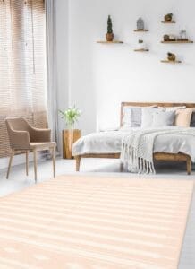 Een moderne, minimalistische slaapkamer met een houten bed, wit beddengoed, een beige fauteuil, een klein bijzettafeltje met een plant, zwevende planken met decor en een groot vloerkleed met een geometrisch patroon.