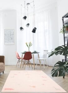 Een moderne, zonovergoten eethoek met een houten tafel, rode en witte stoelen, een hanglamp, potplanten en een lichtgekleurd vloerkleed met dierenpatronen.