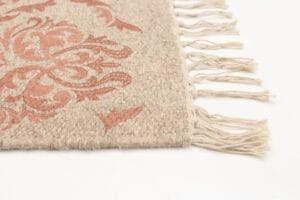 Een close-up van een beige geweven hoekkleed met rode bloemenpatronen en franjekwastjes op een witte achtergrond.