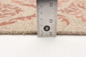 Met een metalen liniaal kunt u de dikte van een beige tapijt met patroon meten. Deze bedraagt ongeveer 23 millimeter.