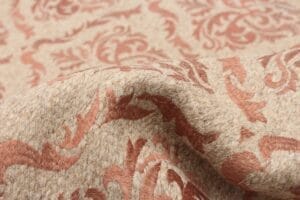 Close-up van beige en rode stof met een bloemenpatroon, waarbij de textuur en vouwen zichtbaar zijn.