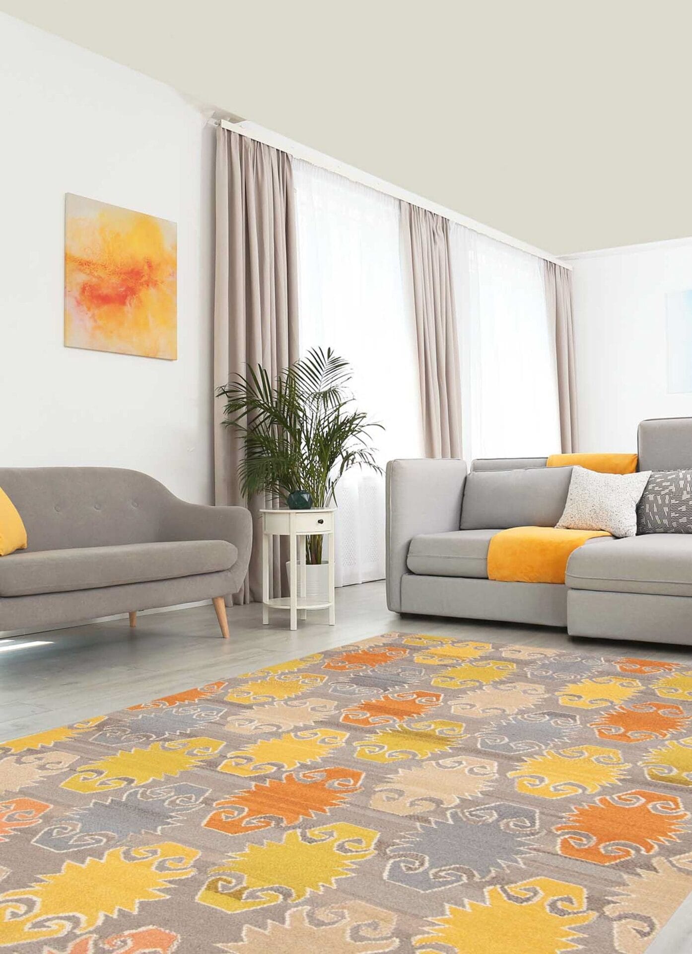 Een moderne woonkamer met een grijze bank en loveseat, gele en grijze kussens, twee kunstwerken aan de muur, een potplant en een geel, grijs en oranje vloerkleed met een patroon.