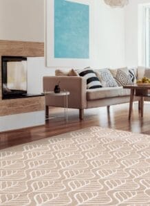 Een moderne woonkamer met een beige bank, een patroonkleed, blauwe wandkunst en een open haard. Een glazen salontafel met een drankje; een schaal met citroenen staat op een bijzettafel.