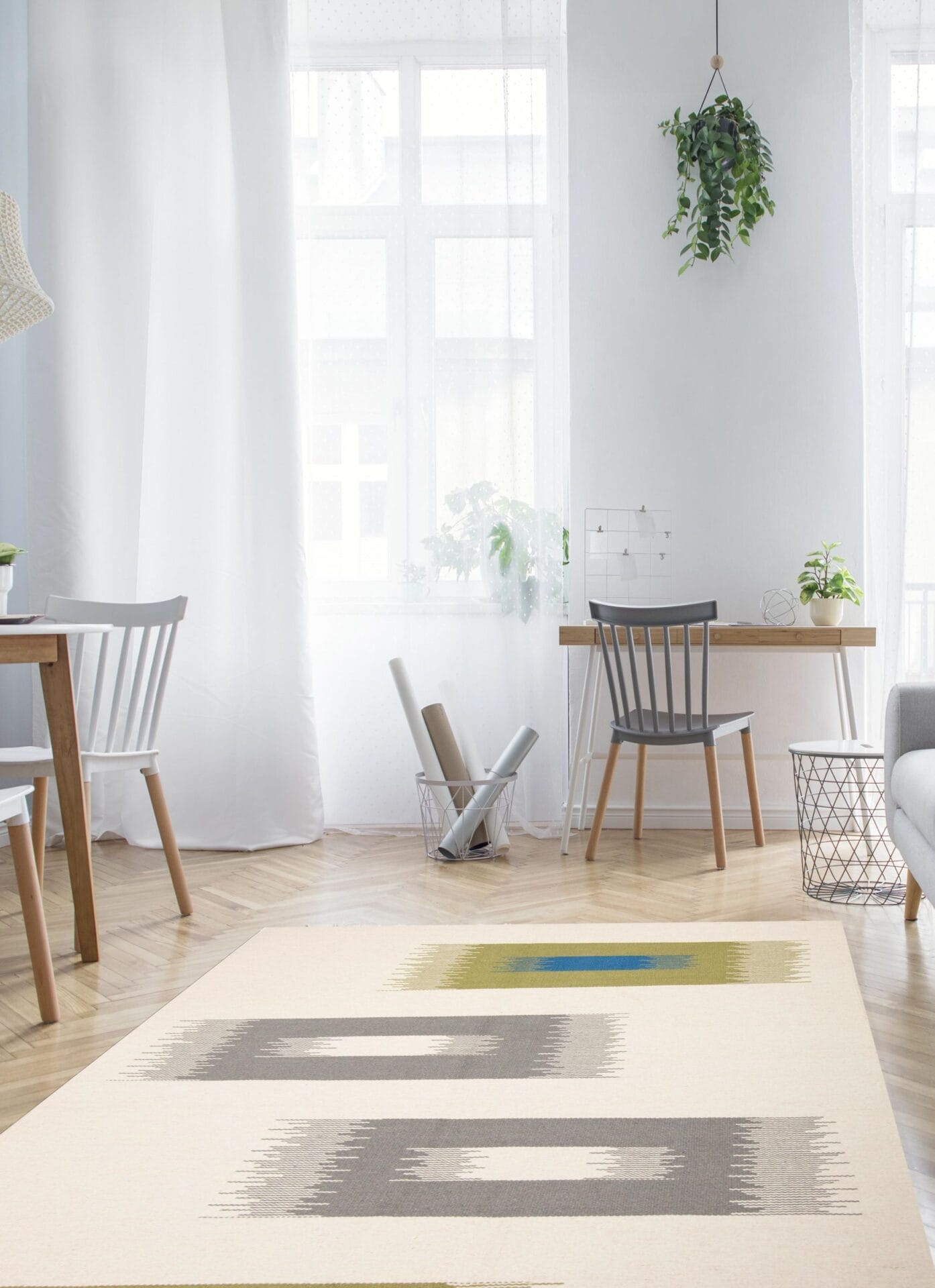 Een lichte, minimalistische kamer met een tapijt met patroon, twee houten stoelen, een bureau bij een raam met witte gordijnen en potplanten.